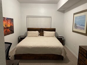 Une chambre à coucher comprenant un lit, deux tables de chevet, une chaise, une commode et deux tableaux encadrés accrochés aux murs.