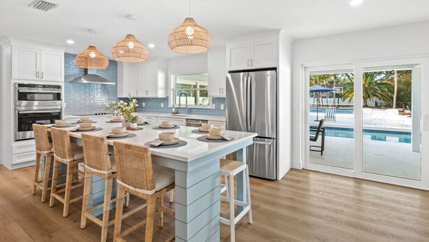 Een moderne keuken met een centraal eiland, barkrukken en uitzicht op een zwembad.