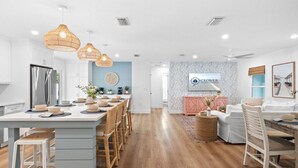 Een moderne keuken met een centraal kookeiland, houten stoelen en hangende rieten hanglampen.