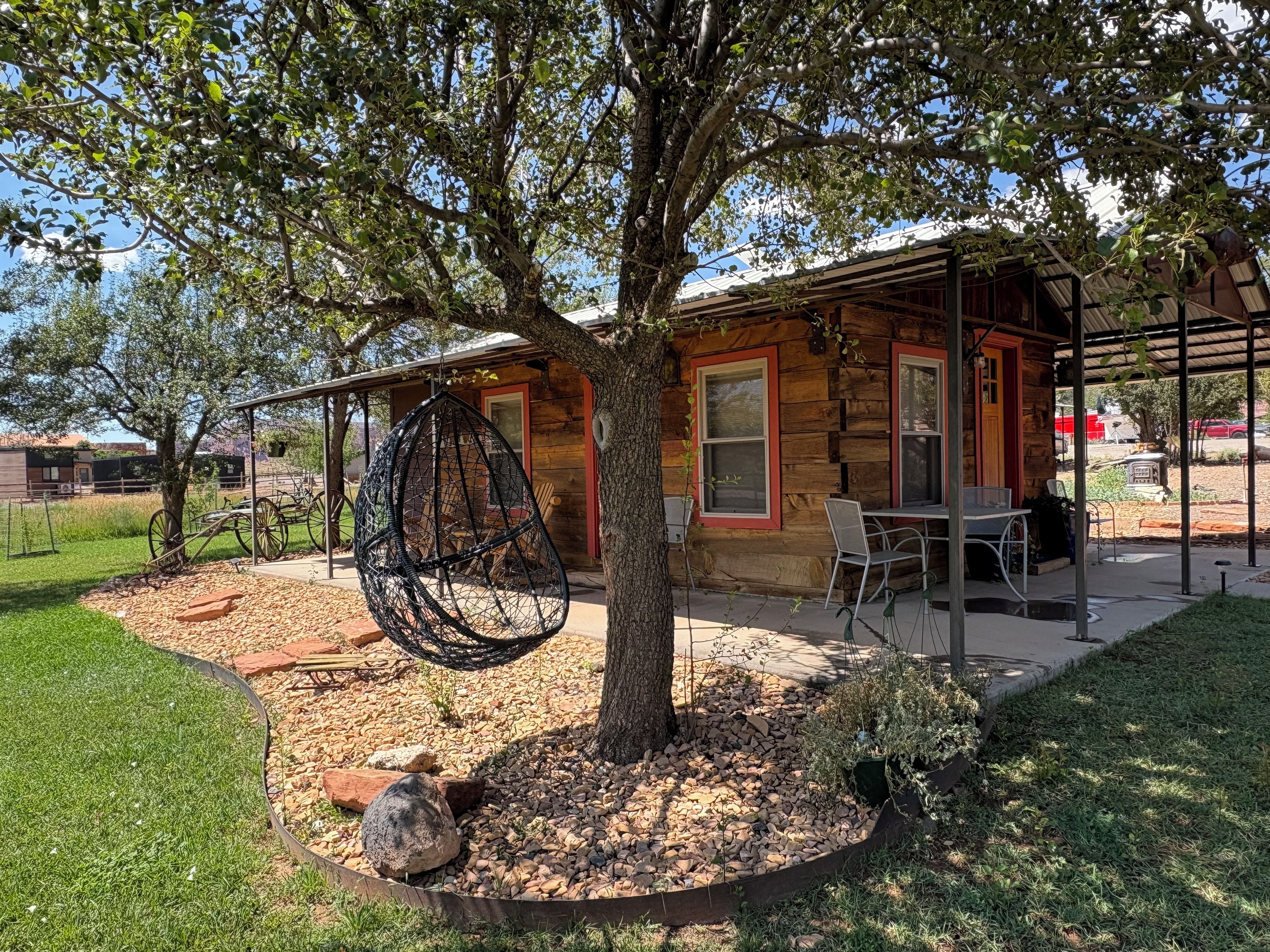 A wooden cabin with a patio area, a hanging chair, and a table with chairs.
