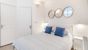 Quarto com cama, duas mesas de cabeceira, um criado-mudo e um guarda-roupa, além de três espelhos fixados na parede.