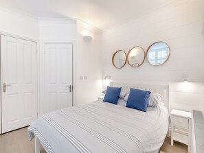 Un dormitorio con cama, dos mesitas de noche, un aparador y tres espejos adosados a la pared.