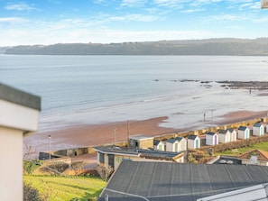 Vista costera con playa, una hilera de cabañas de playa y una zona verde con un edificio en primer plano.