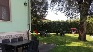 An outdoor patio with a table and chairs, a swing set, and a hedge in the background. - Franco house with pool (Orentano)