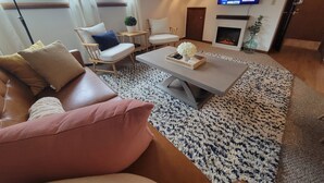 Un salon avec un canapé en cuir marron, une table basse sur laquelle se trouve un plateau avec divers objets, une cheminée et un téléviseur fixé au mur.