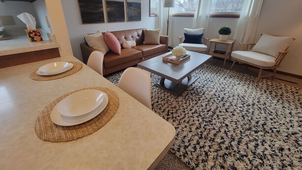 Un salon moderne avec un canapé en cuir marron, un fauteuil blanc, une table basse et un coin repas comprenant une table et des chaises.