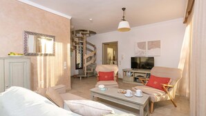 Un salon comprenant un canapé, des fauteuils, une table basse, un téléviseur et un escalier en colimaçon.