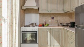 Une cuisine compacte équipée d’une cuisinière, d’un four et d’un évier, avec des meubles de couleur claire en bois et un dosseret carrelé.