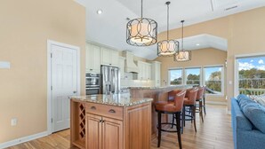 A modern kitchen with a central island, bar stools, and pendant lighting. - Waterfront,Pool,Game Room,Beach,DeepWaterAccess (Manteo)