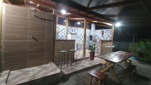 Eine Terrasse im Freien mit einem Holztisch, Hockstühlen und einem Grill.