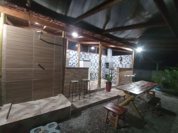 Un patio al aire libre con una mesa de madera, taburetes y una parrilla.