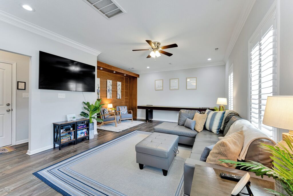 A modern living room with a sectional sofa, a coffee table, a TV mounted on the wall, and a ceiling fan.