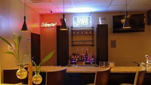 A bar area with a neon sign, shelves with bottles, and a TV mounted on the wall. - Home Inn Woods Hotel (Olive Branch)