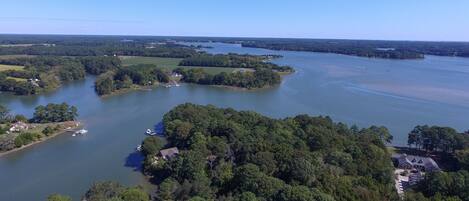 Vue aérienne d’une propriété au bord du lac, dotée de plusieurs quais, et entourée de forêts denses et de vastes champs.
