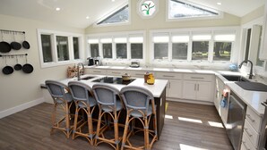 A kitchen with a central island, four bar stools, a hanging pot rack, and a large window with multiple panes. - Pet-Friendly Waterfront Retreat w/ Private Dock on Virginia’s Eastern Shore (Exmore)