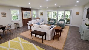 A spacious living room with a white sofa, a coffee table, and a dining area with a table and chairs. There are large windows and a sliding glass door leading to a balcony. - Pet-Friendly Waterfront Retreat w/ Private Dock on Virginia’s Eastern Shore (Exmore)