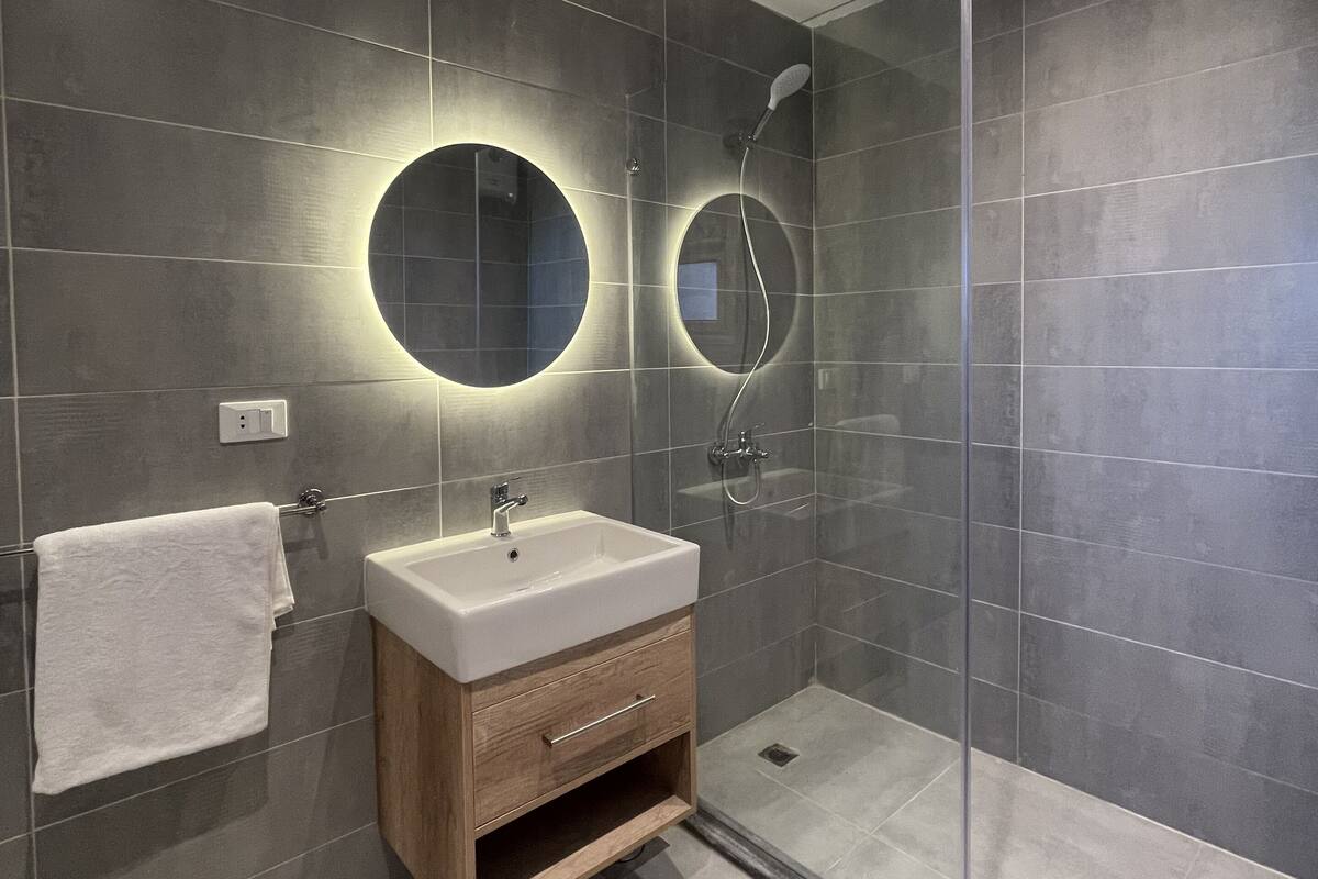 Un bany modern amb una cabina de dutxa de vidre, un tocador de fusta amb un rentapeus blanc i dos miralls circulars penjats a la paret.