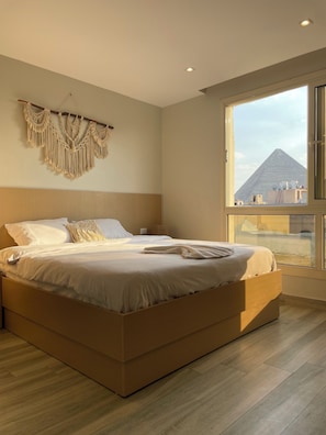 Camera da letto moderna con un letto grande, decorazioni in macramè a parete e vista su una piramide attraverso un'ampia finestra.