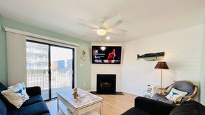 Ein Wohnzimmer mit Fernseher, Kamin, Deckenventilator und Blick auf den Balkon.