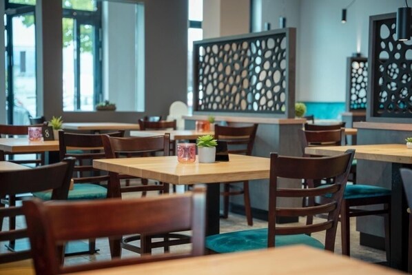 Interior de restaurante con mesas y sillas de madera, paneles decorativos y plantas en macetas.