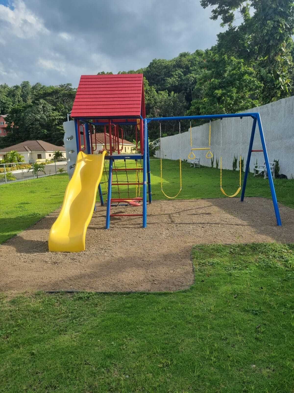 A playground with a red-roofed climbing structure, a yellow slide, and blue swings.