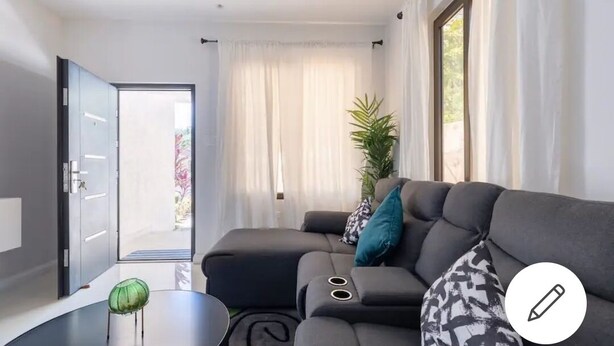 Un salon moderne avec un canapé d’angle, une petite table ronde et une plante en pot.