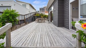 En træterrasse med et bord og stole, omgivet af huse med forskellig facadebeklædning.