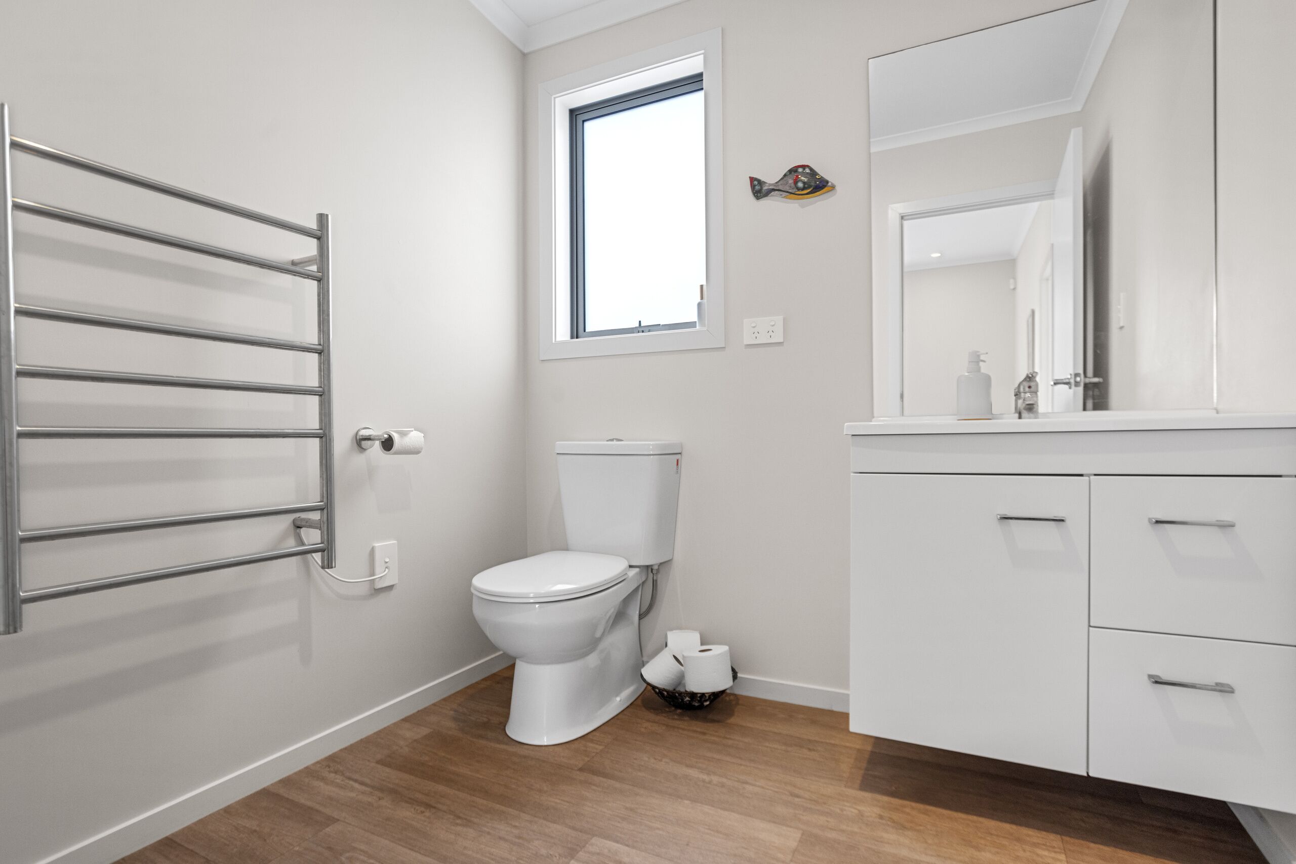 Un baño moderno con inodoro, toallero, ventana y espejo.