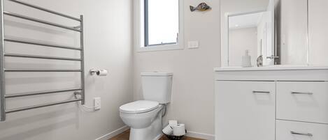 Un baño moderno con inodoro, toallero, ventana y espejo.