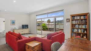 En moderne stue med røde sofaer, et træ sofabord, en reol og en stor skydedør, der fører ud til en terrasse.