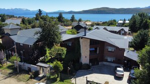 A residential area with houses, a parking area, and a view of a lake with mountains in the background. - COMPLEJO RAICES PATAGONICAS CABAÑA CLASICA (Dina Huapi)