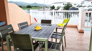 Une terrasse en bois avec une table et des chaises, d’où l’on a vue sur une étendue d’eau, avec des bateaux et des maisons en arrière-plan.