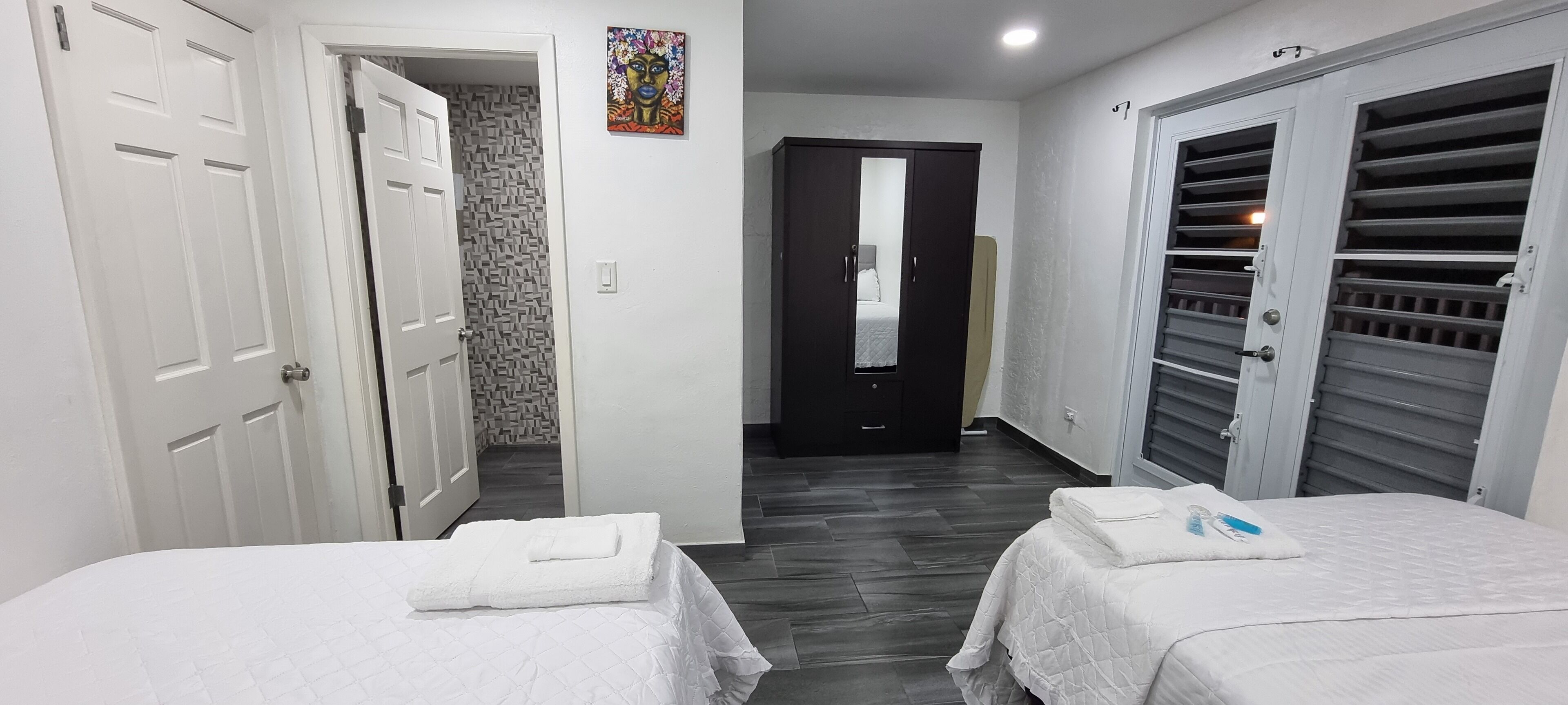Una habitació d'hotel amb dos llits, un armari, un bany i un passadís que condueix a una altra habitació.