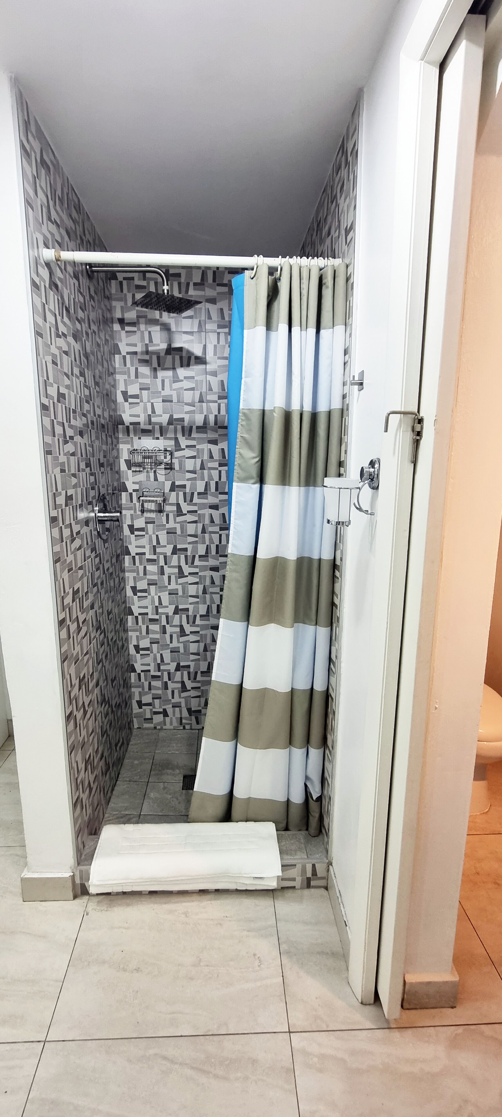 A shower area with a patterned wall, a striped shower curtain, and a small step leading into the shower.