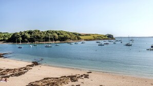 A beach with boats, a sandy shore, and a forested hill.