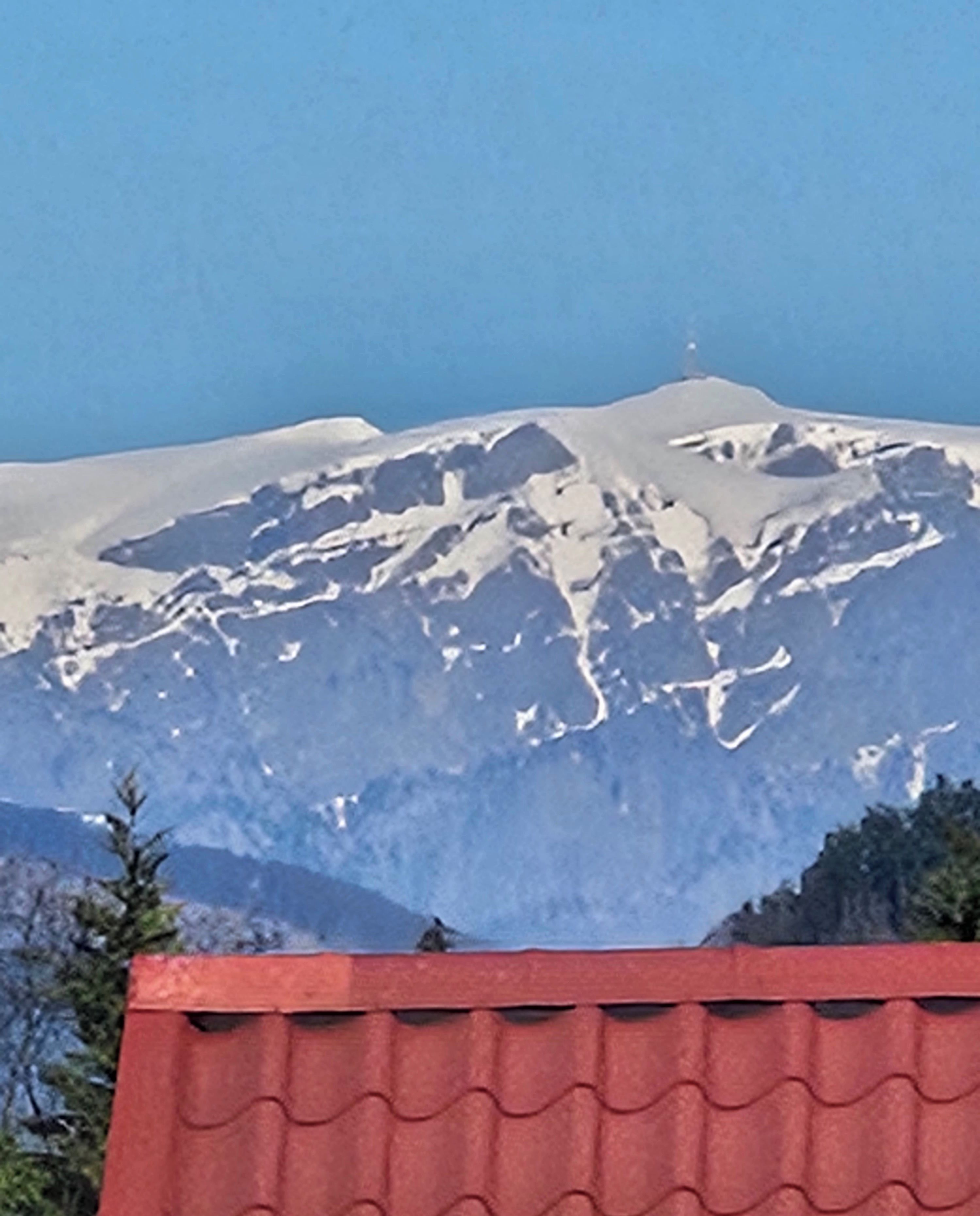A mountain with snow-covered peaks and a red-roofed building in the foreground.