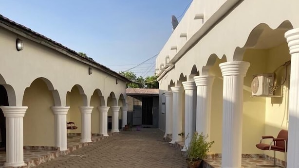 A courtyard with a tiled floor, white columns, and a covered walkway. - Star Lodge  (Farafenni)