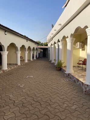 A courtyard with a tiled floor, white columns, and a covered walkway. - Star Lodge  (Farafenni)