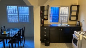 A compact kitchen with a dining area, featuring a stove, sink, and a small trash bin. - Star Lodge  (Farafenni)