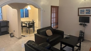 A living room with a sofa, a coffee table, a TV, and a dining area with a table and chairs. - Star Lodge  (Farafenni)