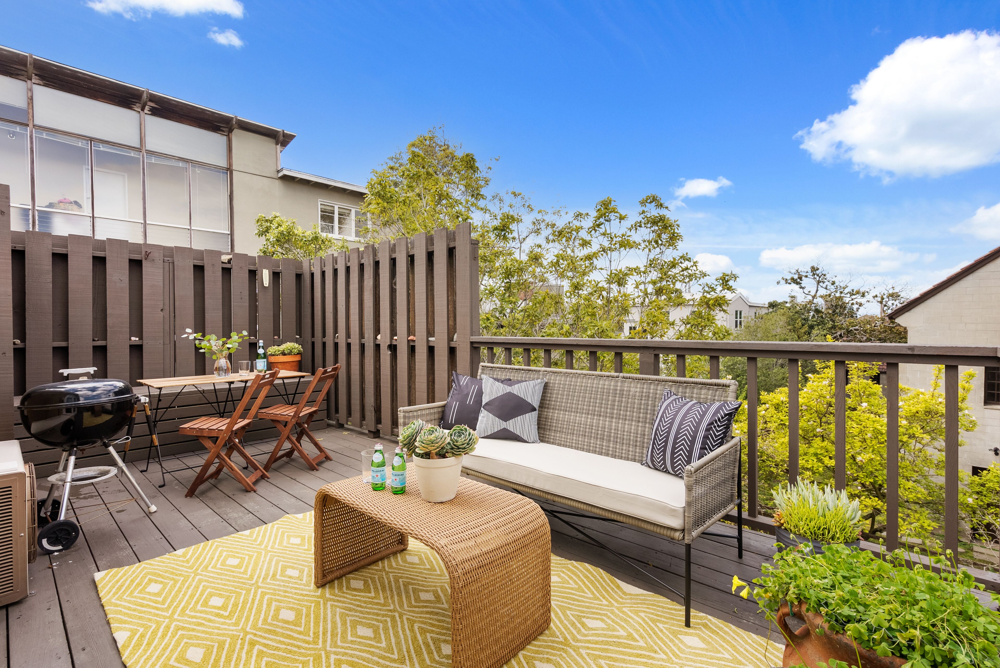 A deck with a grill, seating area, and potted plants.