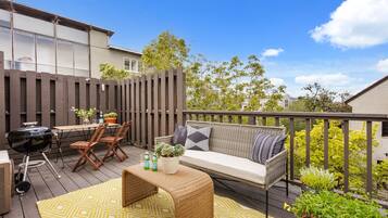 A deck with a grill, seating area, and potted plants.