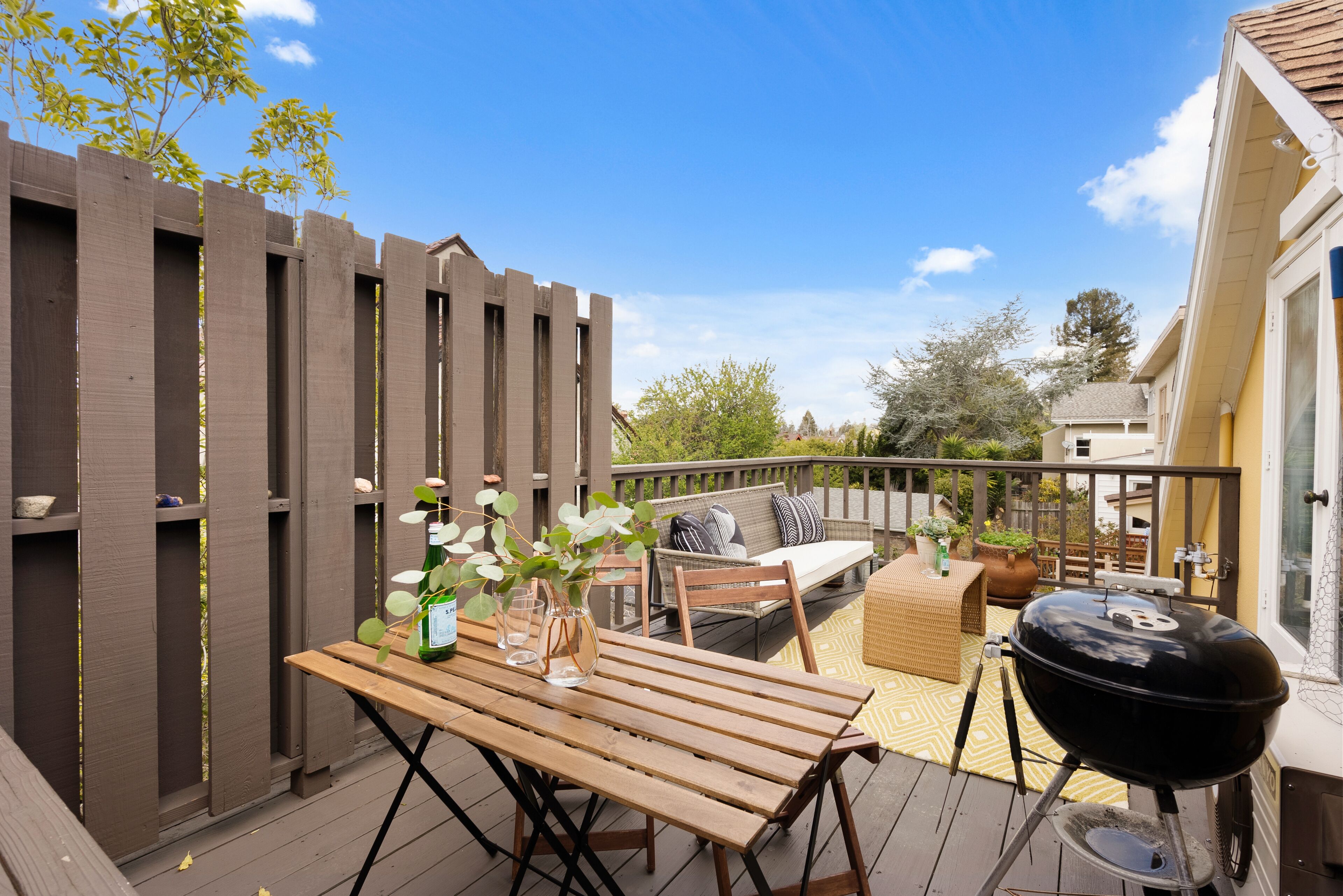 A wooden deck with a table, chairs, a grill, and a sofa.