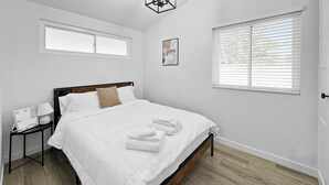 A bedroom with a bed, a nightstand, a wall clock, a window, and a door.