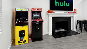 A living room with two arcade machines, a fireplace, and a large flat-screen TV displaying 'hulu'.