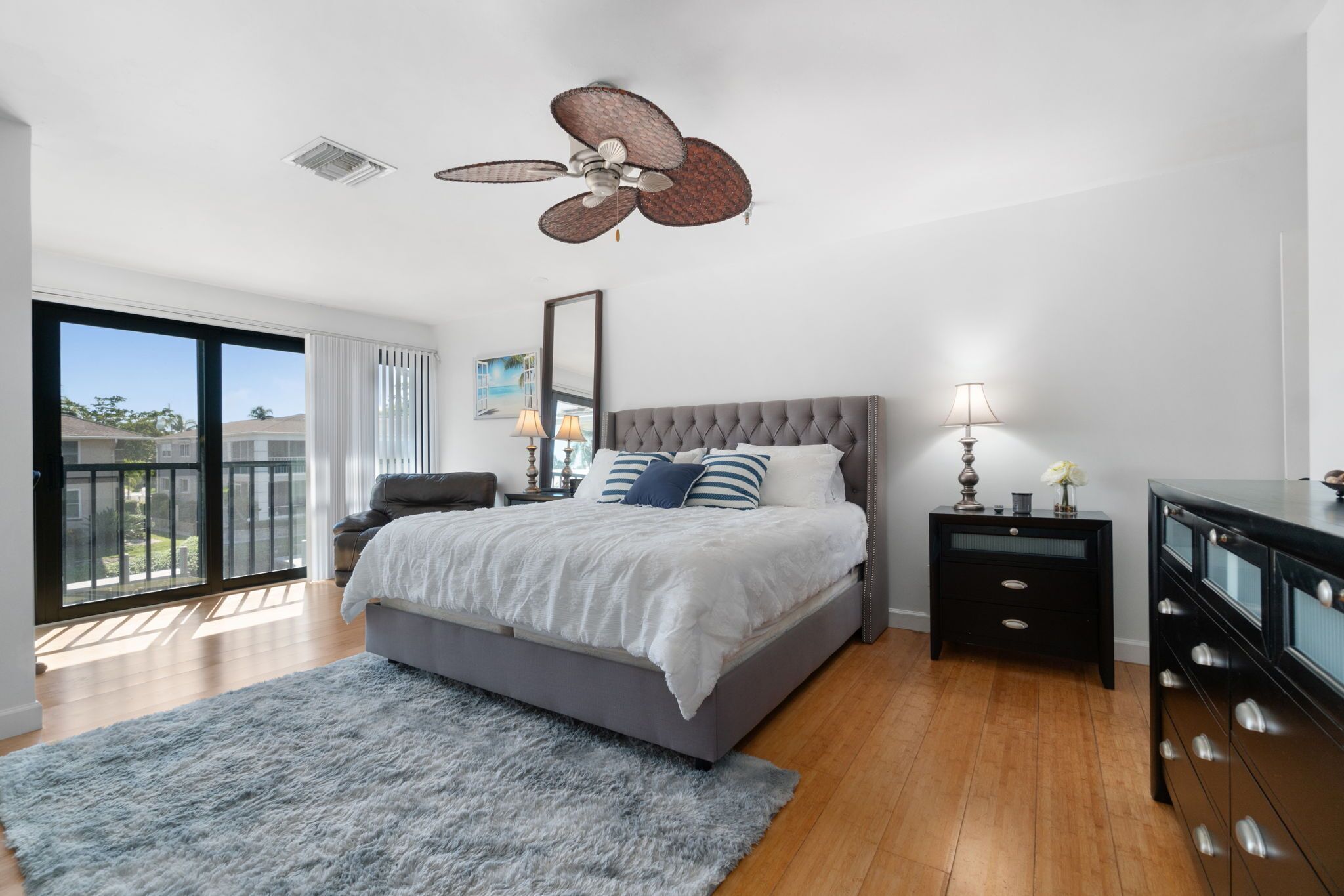 A bedroom with a large bed, a ceiling fan, a dresser, and a view of the outside.