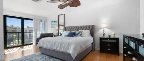 A bedroom with a large bed, a ceiling fan, a dresser, and a view of the outside.