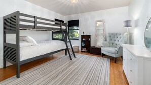 Camera con letto a castello, una scala, un grande specchio, una poltrona capitonné e una cassettiera bianca.