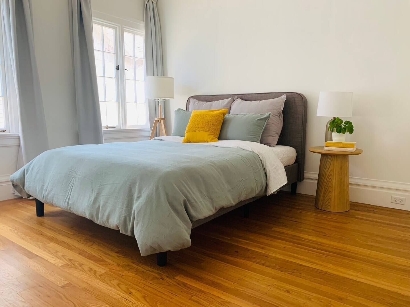 Une chambre à coucher avec un lit, deux tables de chevet, une fenêtre avec des rideaux et un plancher en bois.