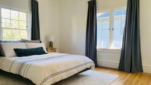 Une chambre à coucher avec un lit, une table de chevet, une lampe et une vue sur l’extérieur par une fenêtre.